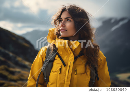 Portrait of a beautiful young woman in yellow jacket with a backpack against the backdrop of picturesque mountains. Female tourist is engaged in hiking. Active lifestyle, travel and trekking concept. Portrait of a beautiful young woman in yellow jacket with a backpack against the backdrop of picturesque mountains. Female tourist is engaged in hiking. Active lifestyle, travel and trekking concept. 108020049