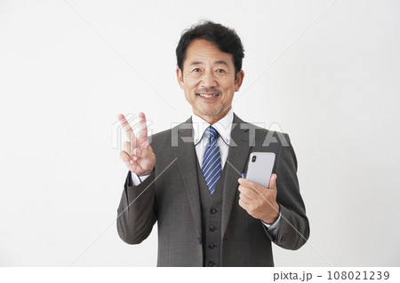 スマートフォンを持ってピースサインをする中年のビジネスマン　白背景 108021239