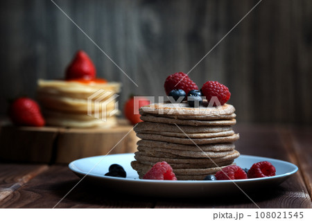 A stack of pancakes with fresh raspberries and blueberries on a light plate on a wooden background 108021545