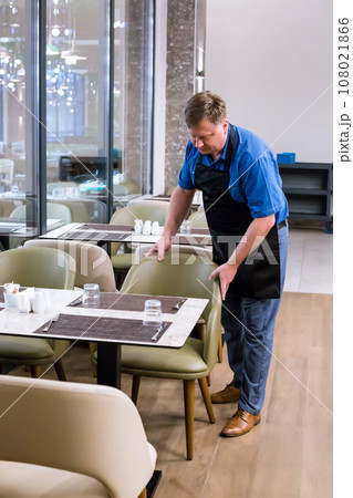 The owner of the cafe arranges chairs and tables before starting work 108021866