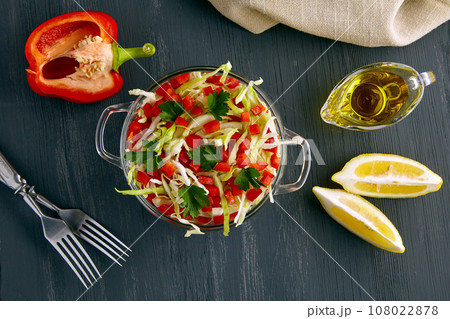 An appetizing light salad of white cabbage, bell pepper and parsley dressed with a mixture of olive oil and lemon in a glass bowl surrounded by ingredients on a black wooden table An appetizing light salad of white cabbage, bell pepper and parsley dressed with a mixture of olive oil and lemon in a glass bowl surrounded by ingredients on a black wooden table 108022878