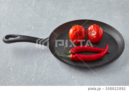 Fried tomatoes and hot capsicums are laid out in the shape of a smiley face on a black cast iron frying pan 108022892