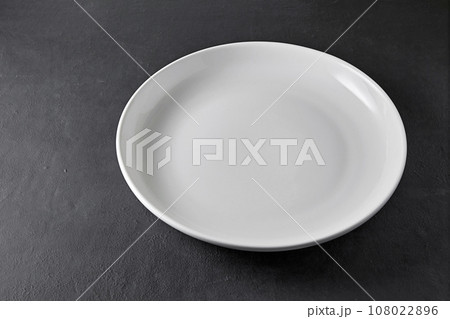 White ceramic plate on a black stone table. Empty plate to display food in restaurant menu 108022896
