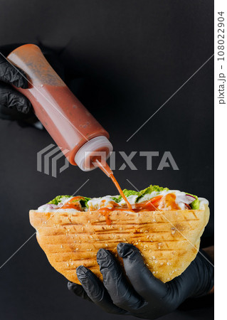 Cooks hand adding sauce to doner kebab through torn holes on black paper background Cooks hand adding sauce to doner kebab through torn holes on black paper background 108022904