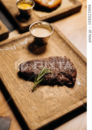 Fresh juicy delicious beef steak on wooden background in restaurant. Meat dish with spices and herbs Fresh juicy delicious beef steak on wooden background in restaurant. Meat dish with spices and herbs 108023906