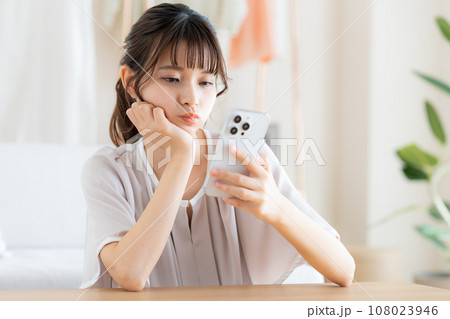 リビングでスマホを見る若い女性 108023946