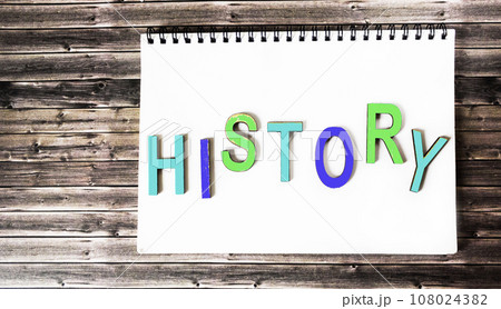 The word history is written in multicolored wooden letters on a white notebook. Wooden background. 108024382