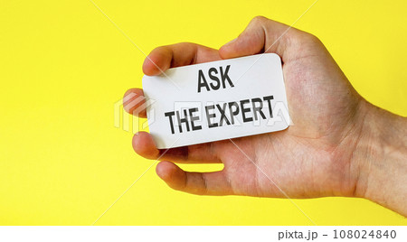 Businessman holds a card with the text ask the expert on a yellow background Businessman holds a card with the text ask the expert on a yellow background 108024840