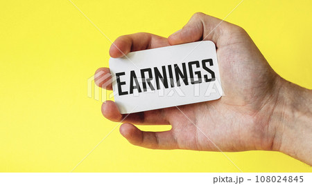 Hand holds a card with the word earnings on a yellow background Hand holds a card with the word earnings on a yellow background 108024845