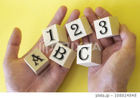 Hands holding cubes on a yellow background with the text 1 2 3 A B C Hands holding cubes on a yellow background with the text 1 2 3 A B C 108024848