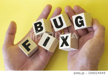 Bug fix, text is written on wooden blocks in male hands on a yellow background 108024849