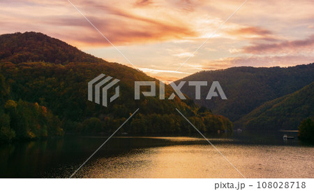 mountainous autumn landscape with lake at dusk. scenery in fall colors reflecting in the calm water. local tourism and relaxation concept. cluj county, romania mountainous autumn landscape with lake at dusk. scenery in fall colors reflecting in the calm water. local tourism and relaxation concept. cluj county, romania 108028718