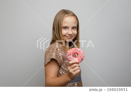 Cheerful child girl posing with pink glazed donut, studio portrait. Holiday birthday party concept 108029051