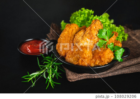 Fast food.Semi-finished chicken wings on a dark background with fresh herbs. Half-finished. Quick cooking at home. Breaded chicken wings.Chicken wings fried until half cooked, semi-finished product. 108029206