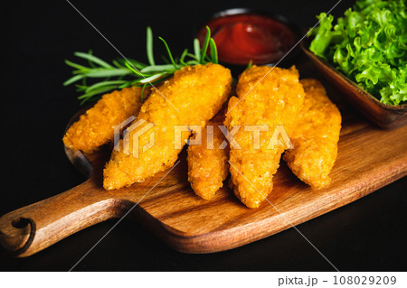 Fast food.Fast cooking.Chicken nuggets with salad.Chicken Breaded Raw Meat.Semifinished Breaded chicken nuggets from chicken fillet on a dark background with fresh herbs. Quick cooking at home. 108029209