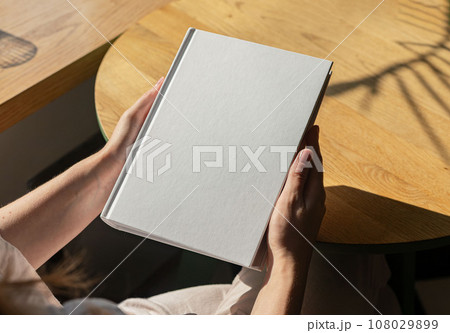 Book mock up, hand holding hard cover mockup on wood table Book mock up, hand holding hard cover mockup on wood table 108029899