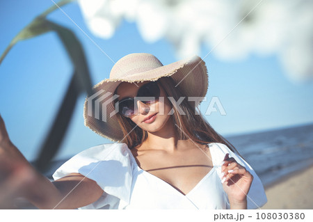 Happy smiling woman is on ocean beach. View through white blurred flowers 108030380