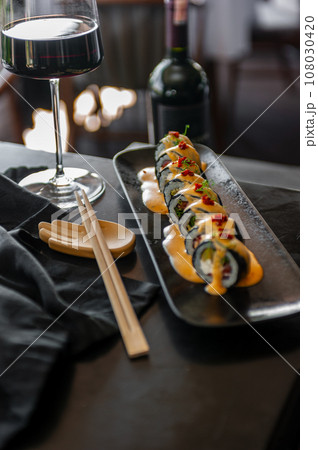 Sushi roll with tuna and vegetables in sauce on a black plate in a restaurant Sushi roll with tuna and vegetables in sauce on a black plate in a restaurant 108030420