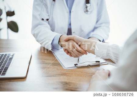 Doctor and patient shaking hands above the wooden table in clinic. Medicine concept 108030726