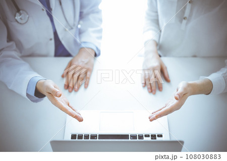 Doctor and patient sitting near each other at the table in clinic. The focus is on female hands pointing into tablet computer touchpad together. Medicine concept Doctor and patient sitting near each other at the table in clinic. The focus is on female hands pointing into tablet computer touchpad together. Medicine concept 108030883