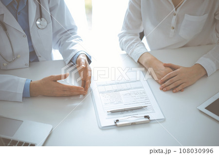 Doctor and patient discussing current health questions while sitting near of each other and using clipboard at the table in clinic, just hands closeup. Medicine concept Doctor and patient discussing current health questions while sitting near of each other and using clipboard at the table in clinic, just hands closeup. Medicine concept 108030996