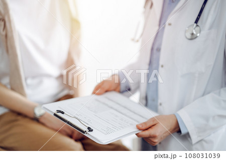 Doctor and patient discussing perfect health exam results. Friendly physician keeping with hands clipboard with medical papers near young woman. Medicine concept 108031039