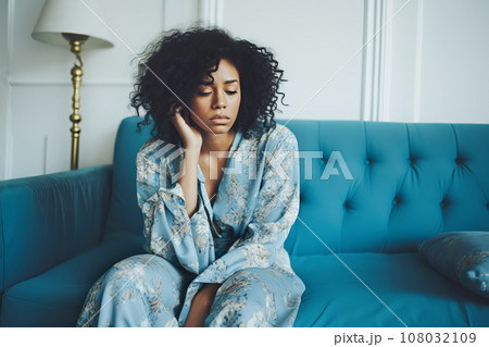 Sad depressed African American woman sitting in pajamas on sofa at home Sad depressed African American woman sitting in pajamas on sofa at home 108032109