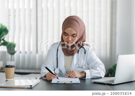 Young muslim female doctor in brown hijab headscarf working with medical papers while sitting in modern clinic office. 108035814