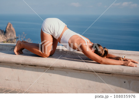 Fitness woman sea. A happy middle aged woman in white sportswear exercises morning outdoors in a park with a beach view. Female fitness pilates yoga routine concept. Healthy lifestyle. Fitness woman sea. A happy middle aged woman in white sportswear exercises morning outdoors in a park with a beach view. Female fitness pilates yoga routine concept. Healthy lifestyle. 108035976
