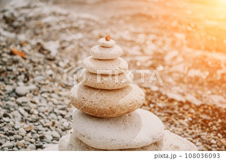 Balanced rock pyramid on sea pebbles beach, at sunset. Golden sea bokeh on background. Selective focus, zen stones on sea beach, meditation, spa, harmony, calm, balance concept 108036093