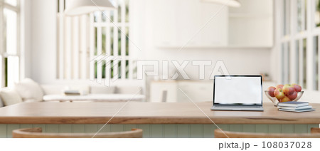 A laptop mockup on a wood kitchen island in a modern white home studio with living room and kitchen. 108037028