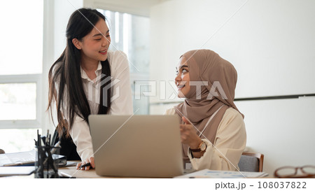 Cheerful Asian businesswoman and her muslim colleague are enjoying sharing their ideas for a project Cheerful Asian businesswoman and her muslim colleague are enjoying sharing their ideas for a project 108037822