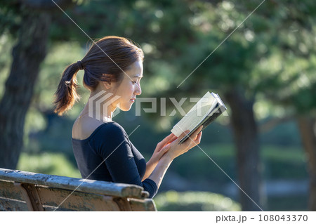 緑に囲まれた公園のベンチで本を読む女性 108043370