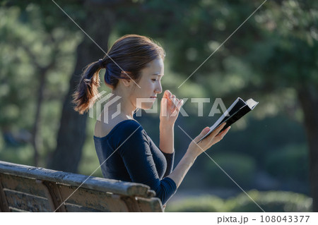 緑に囲まれた公園のベンチで本を読む女性 緑に囲まれた公園のベンチで本を読む女性 108043377