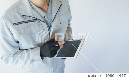 タブレットを持つ作業服の男性　指先がカットされた手袋で操作する 108044447
