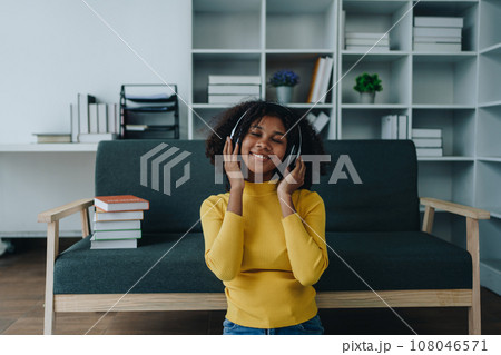 Happy young African American latina woman listening to music using headphones at home living room. relaxing, relax, relaxation concepts. 108046571