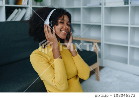 Happy young African American latina woman listening to music using headphones at home living room. relaxing, relax, relaxation concepts. 108046572
