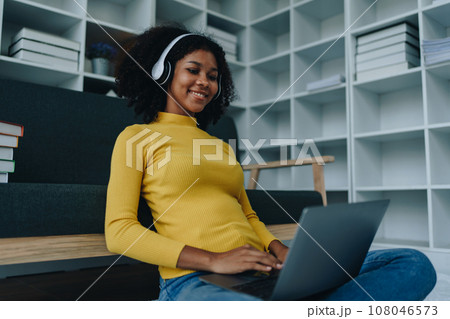 Happy young African American latina woman listening to music using headphones at home living room. relaxing, relax, relaxation concepts. Happy young African American latina woman listening to music using headphones at home living room. relaxing, relax, relaxation concepts. 108046573