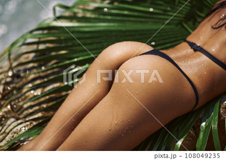 Close-up Female Tanned Back and Buttocks in Black Bikini Rocky Beach  108049235