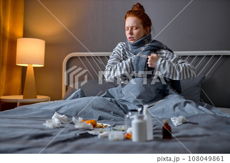 sad ginger girl sitting on bed tablets to reduce symptoms 108049861