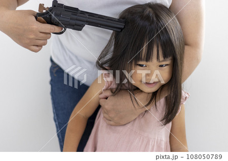 玩具の拳銃を頭に当てられた笑顔の女の子(3歳、日本人) 玩具の拳銃を頭に当てられた笑顔の女の子(3歳、日本人) 108050789