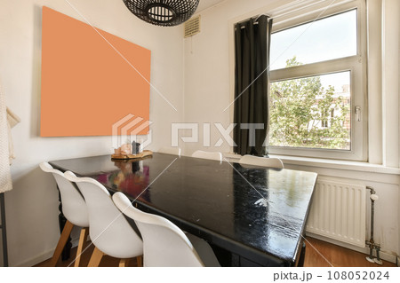 a dining table and chairs in a room with an orange wall art piece on the wall next to the window a dining table and chairs in a room with an orange wall art piece on the wall next to the window 108052024