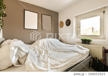 an unmade bed with white sheets and pillows on it in front of a window, next to a plant an unmade bed with white sheets and pillows on it in front of a window, next to a plant 108052025