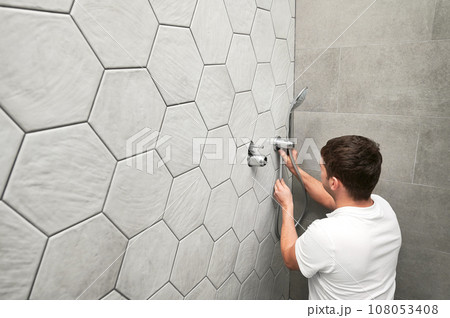 Man plumber installing handheld showerhead in bathroom. Male worker fixing metal bath showerhead and doing plumbing works while working on home renovation. Man plumber installing handheld showerhead in bathroom. Male worker fixing metal bath showerhead and doing plumbing works while working on home renovation. 108053408