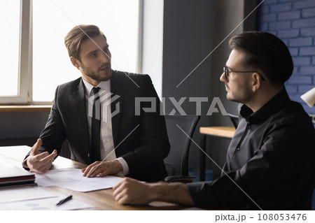 Two businessmen sitting at desk working on project Two businessmen sitting at desk working on project 108053476
