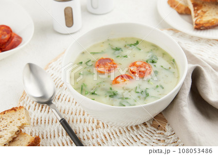 Typical Portuguese soup Caldo Verde with bread and chorizo sausage on gray background 108053486