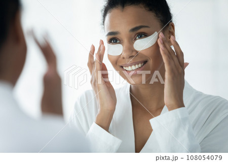Biracial young woman apply under eye patches in bath 108054079