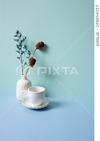 White coffee cup and vase of dry rose flower on blue table. mint green background 108054357