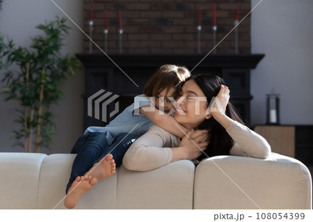 Happy loving Asian mother and son hugging, sitting on couch 108054399