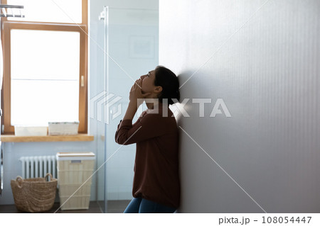 Frustrated depressed Indian woman crying, standing near wall at home 108054447